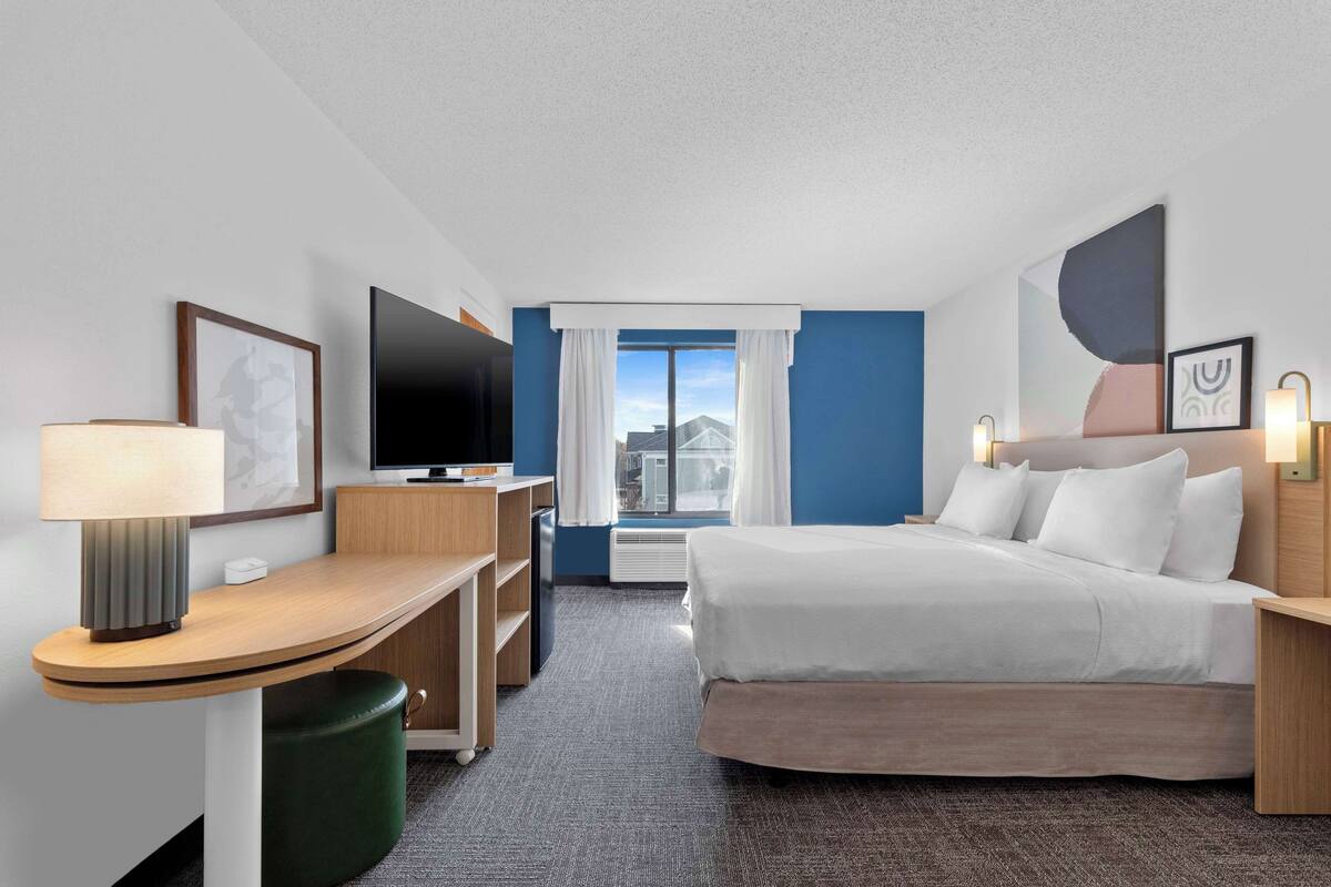 Une chambre d’hôtel avec un lit, un bureau, une télévision et une fenêtre avec des rideaux.
