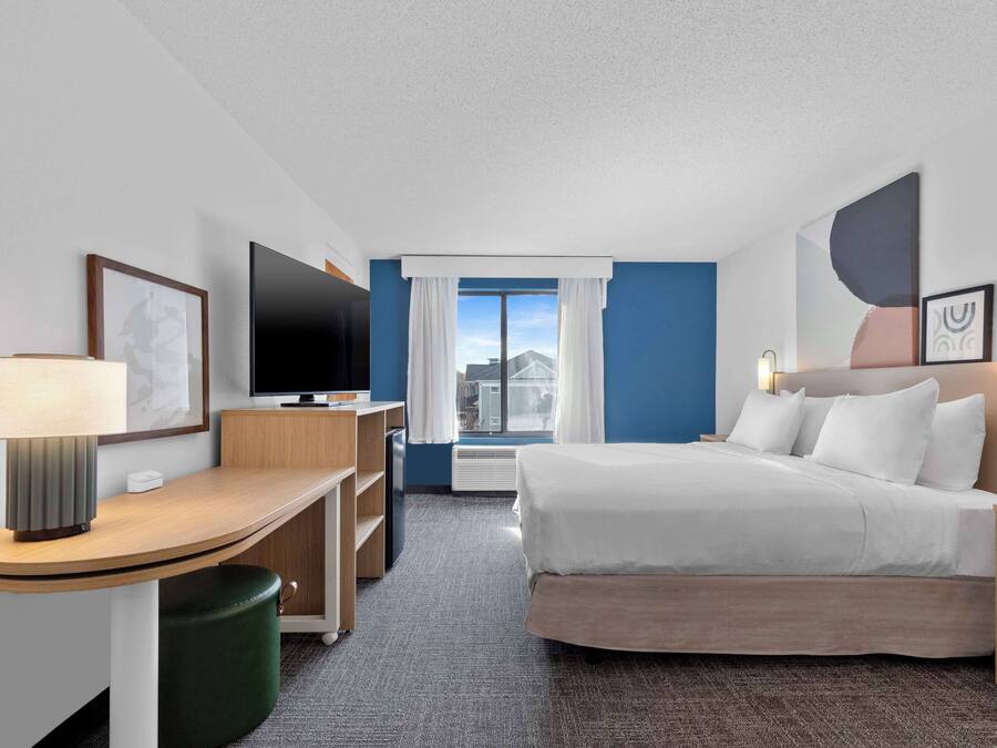 Ett hotellrum med en säng, ett skrivbord, en tv och ett fönster med gardiner.