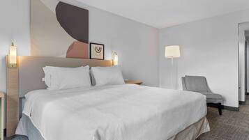 A hotel room with a large bed, two bedside lamps, a chair, and a wall art piece.