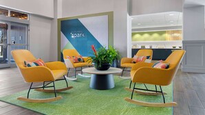 Un hall d’entrée moderne avec des fauteuils à bascule jaunes, une table basse centrale et un grand panneau lumineux en forme d’étincelle.