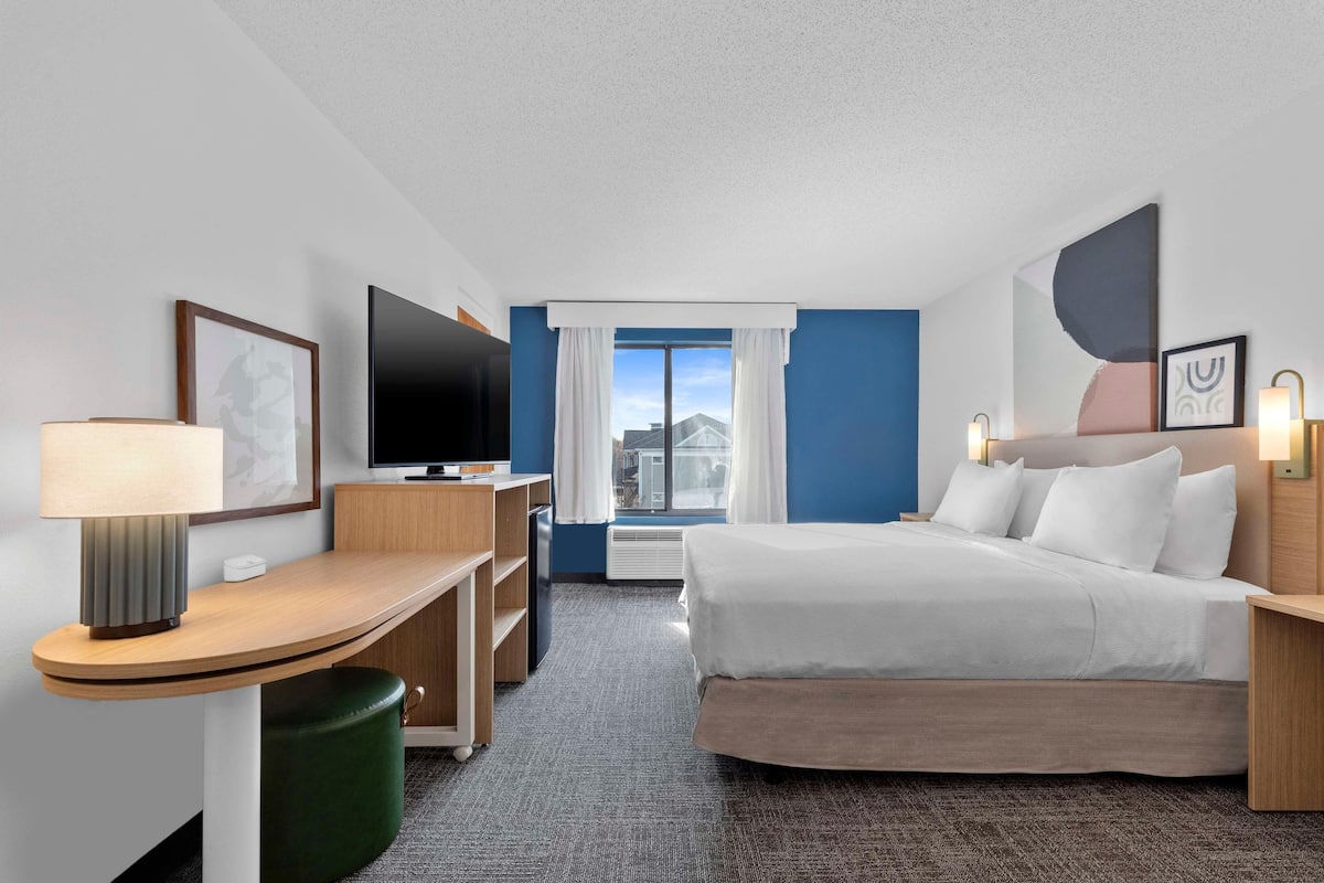 Une chambre d’hôtel avec un lit, un bureau, une télévision et une fenêtre avec des rideaux.