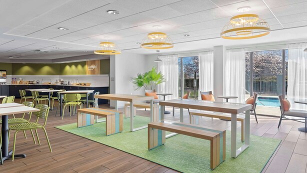 Un espace repas moderne avec des chaises vertes, des tables en bois et une vue sur la piscine.