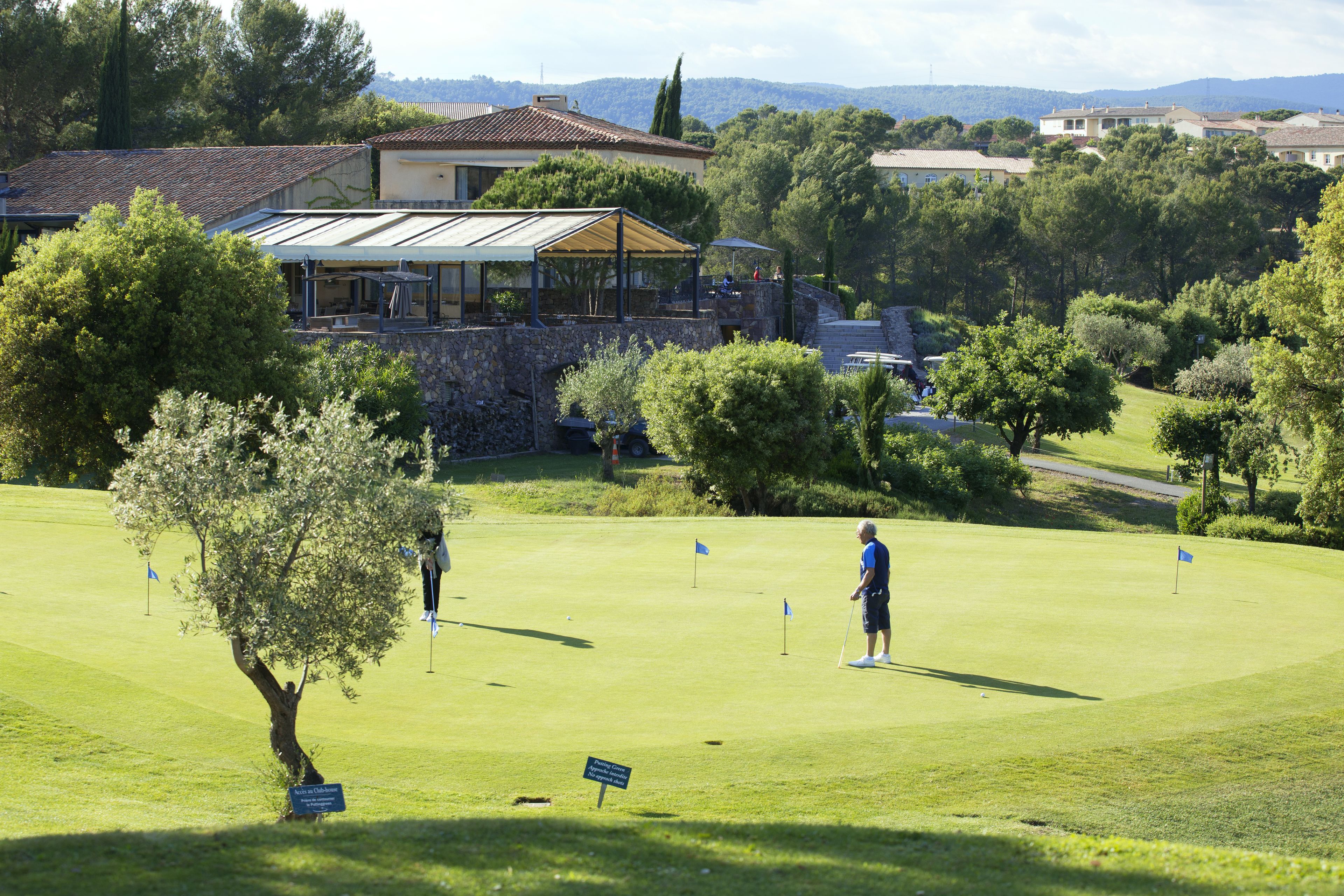 Un campo de golf con un club de campo, árboles y un muro de piedra.