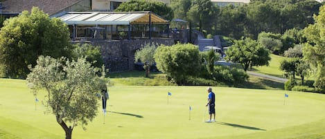 Un campo de golf con un club de campo, árboles y un muro de piedra.