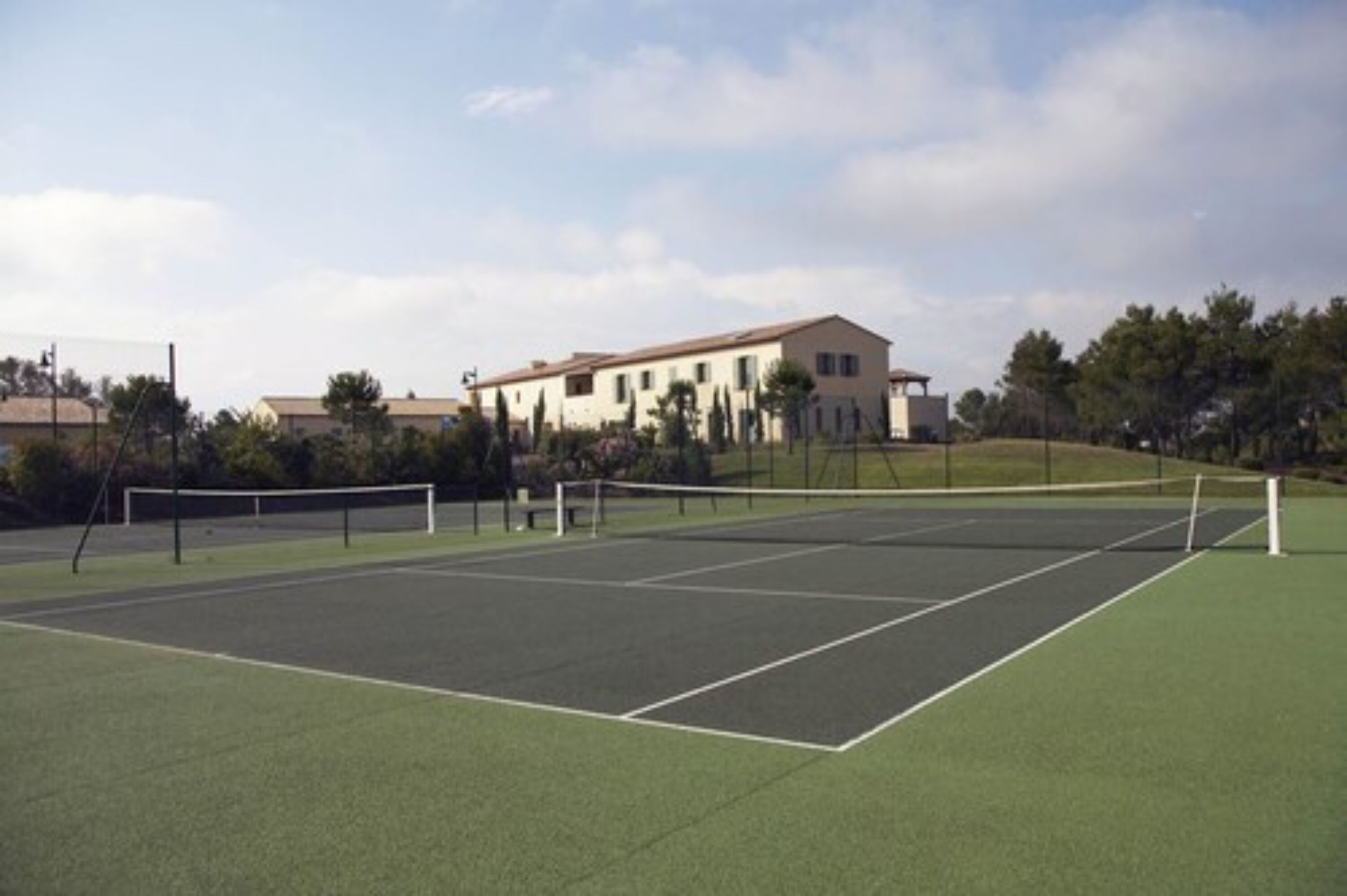 A tennis court with a net, surrounded by a green surface, and a building in the background.