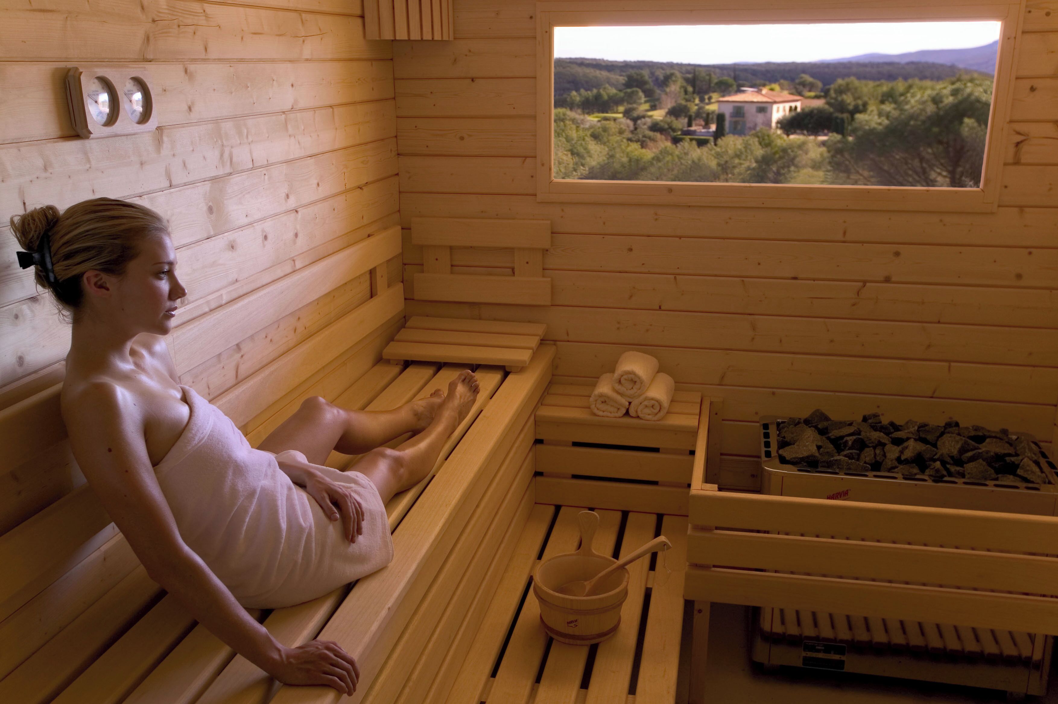 A wooden sauna with a view of the countryside, a bench, a bucket, and towels.
