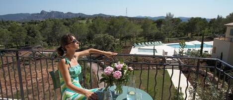 Una mujer sentada en un balcón con una mesa, un jarrón de flores y vistas al paisaje.