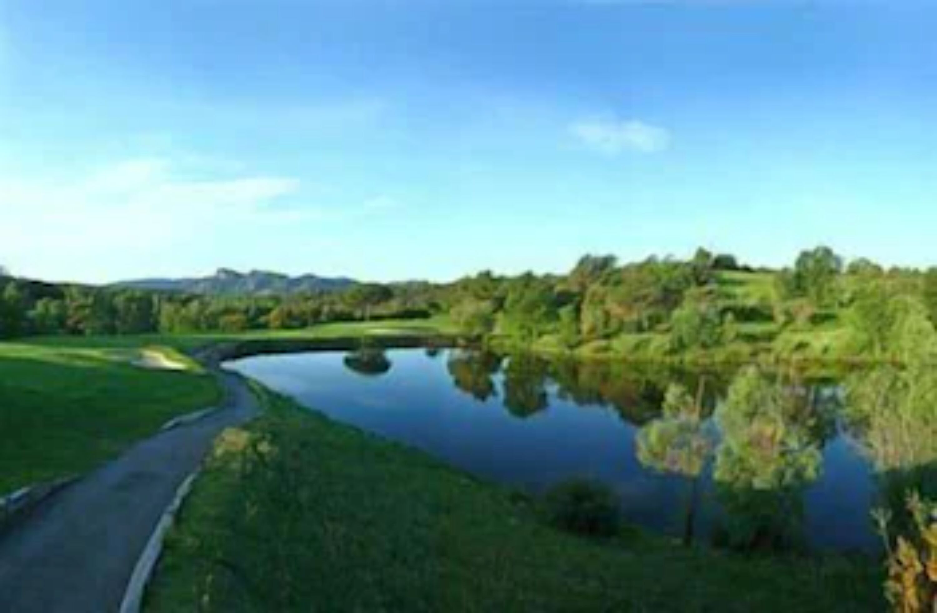 A serene landscape with a calm lake, a winding road, and lush greenery.