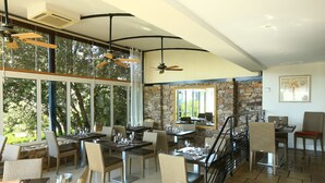 A spacious dining area with high ceilings, large windows, and a stone accent wall. - Domaine de Saint Endréol Golf & Spa Resort**** (La Motte)