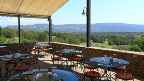 An outdoor dining area with tables and chairs, stone walls, and a view of distant mountains. - Domaine de Saint Endréol Golf & Spa Resort**** (La Motte)