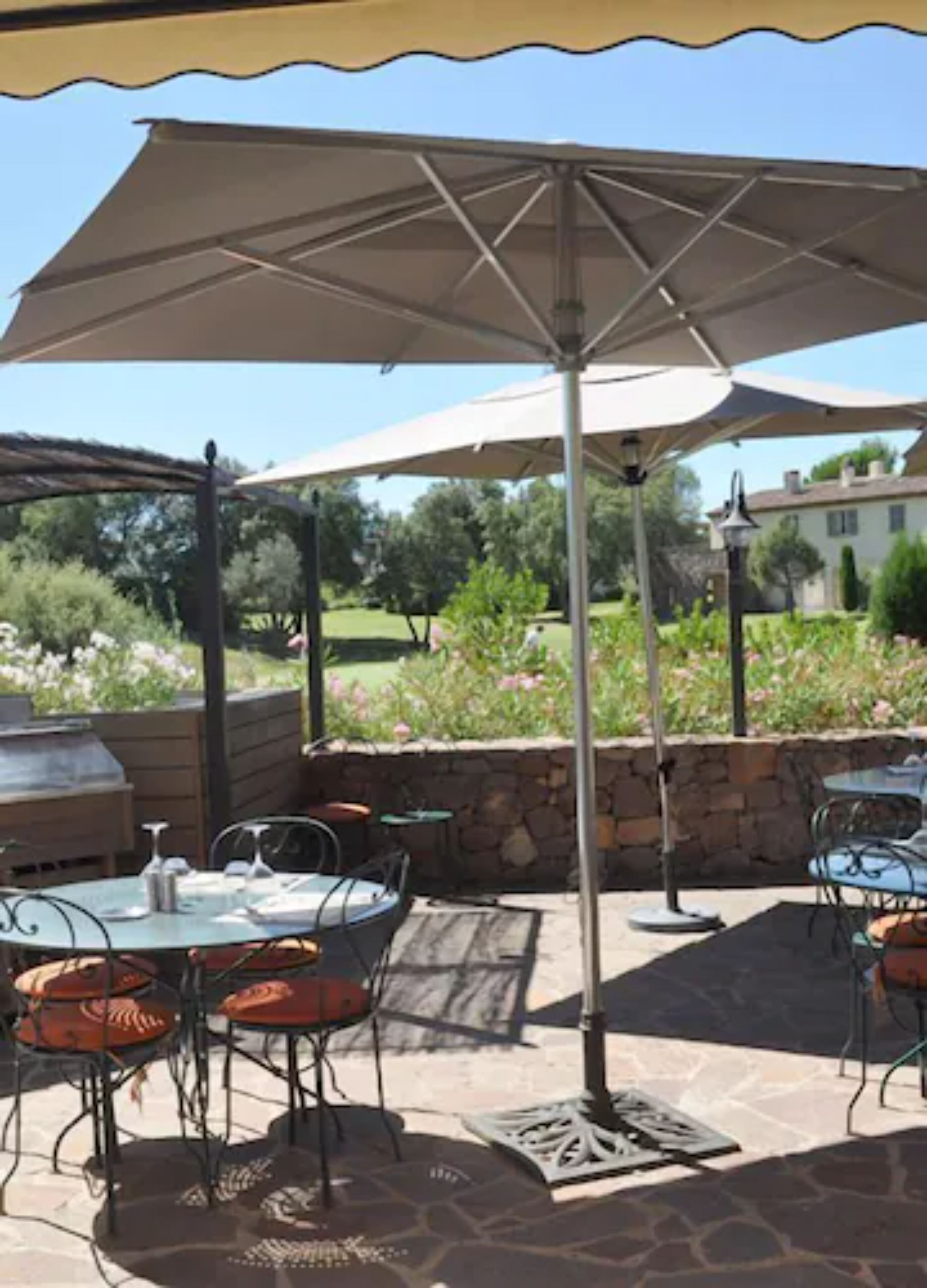 Un patio al aire libre con mesas y sillas, una pérgola y un muro de piedra.