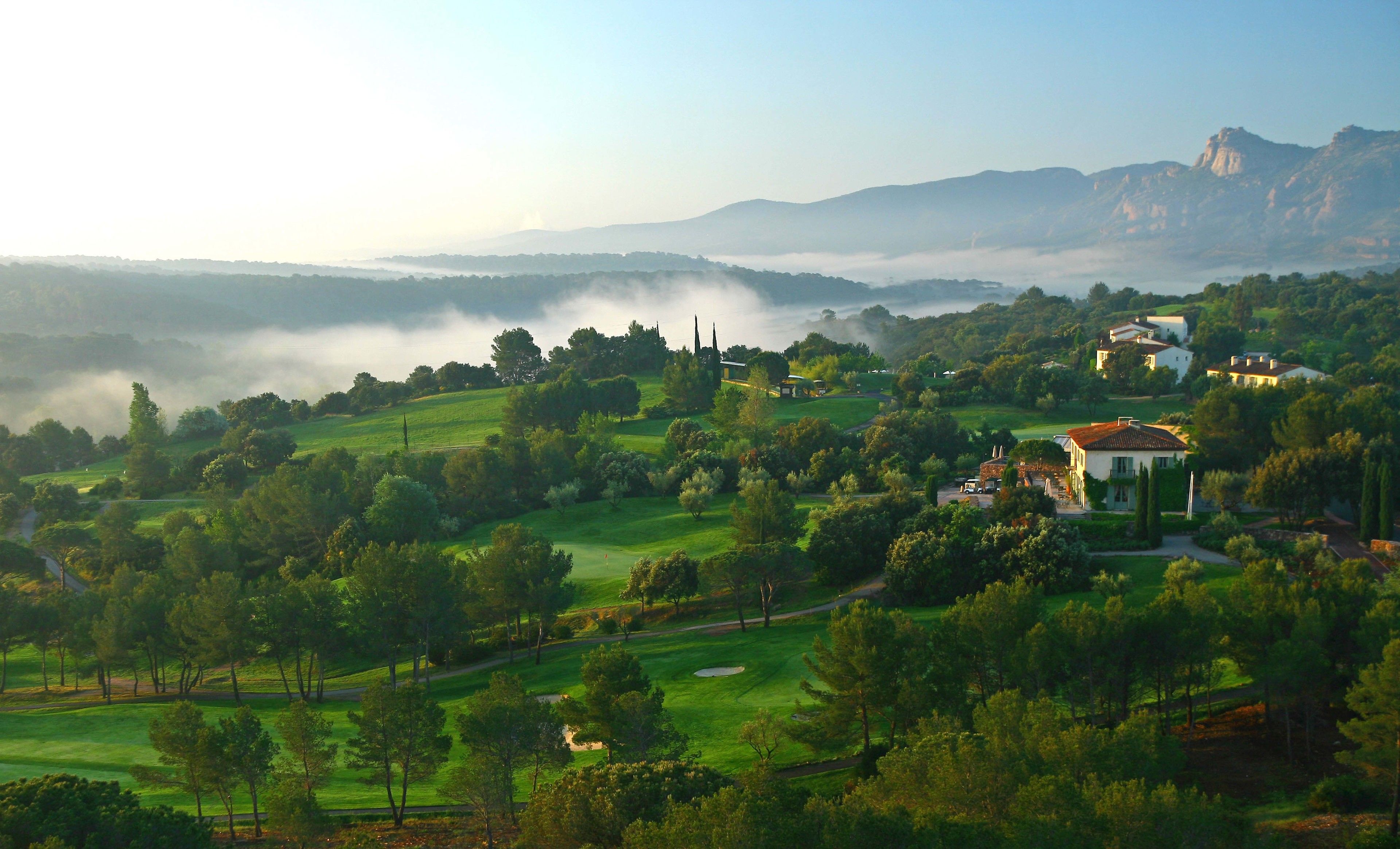 Un campo de golf con un club de campo y árboles circundantes.