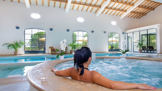 A woman relaxing in a hot tub with a view of a swimming pool and large windows. - Domaine de Saint Endréol Golf & Spa Resort**** (La Motte)