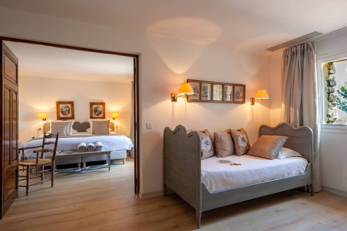 Un dormitorio con cama, una banca y una silla. Hay dos mesitas de noche con lámparas.