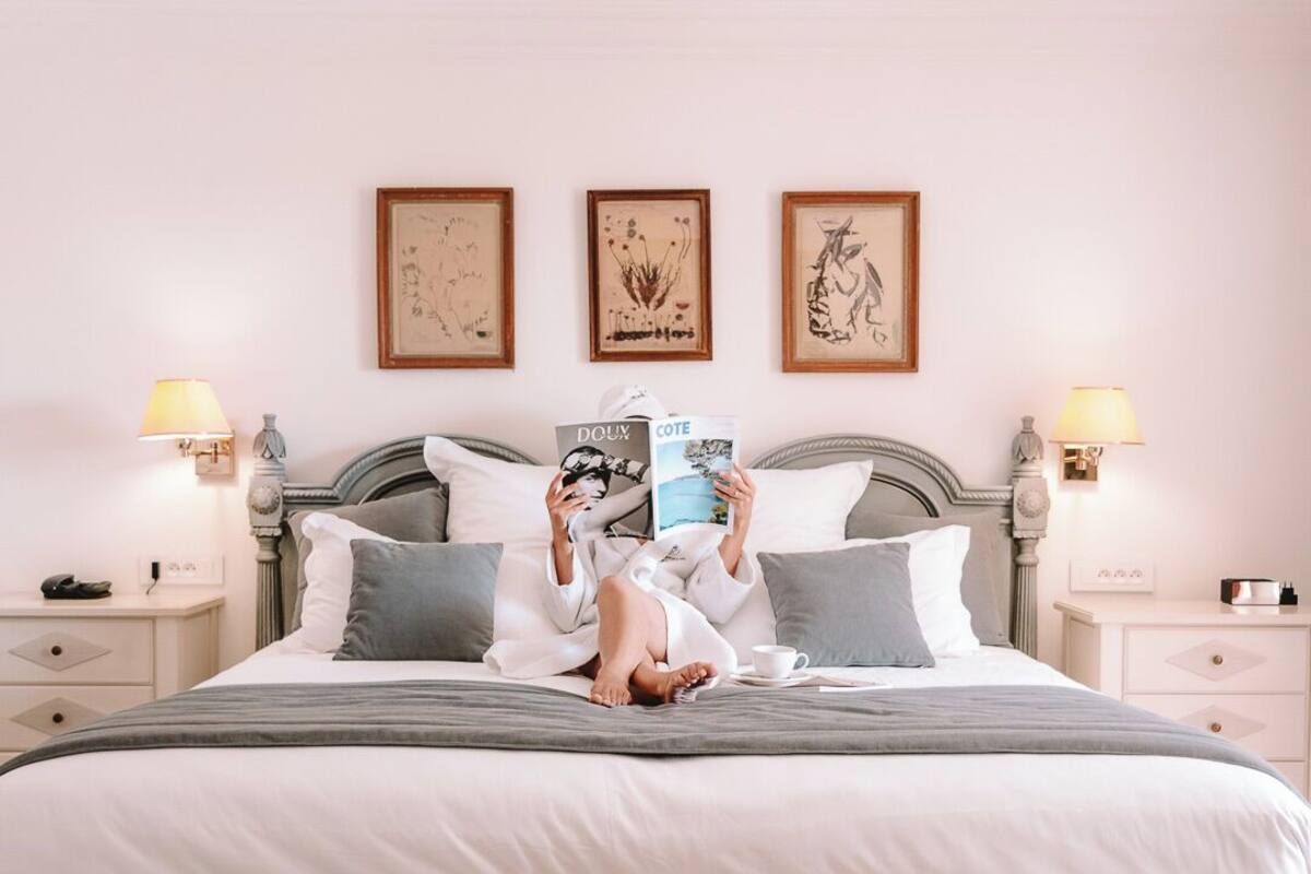 Un dormitorio con cama, mesitas de noche, lámpara de lectura, un banco y cuadros en la pared.