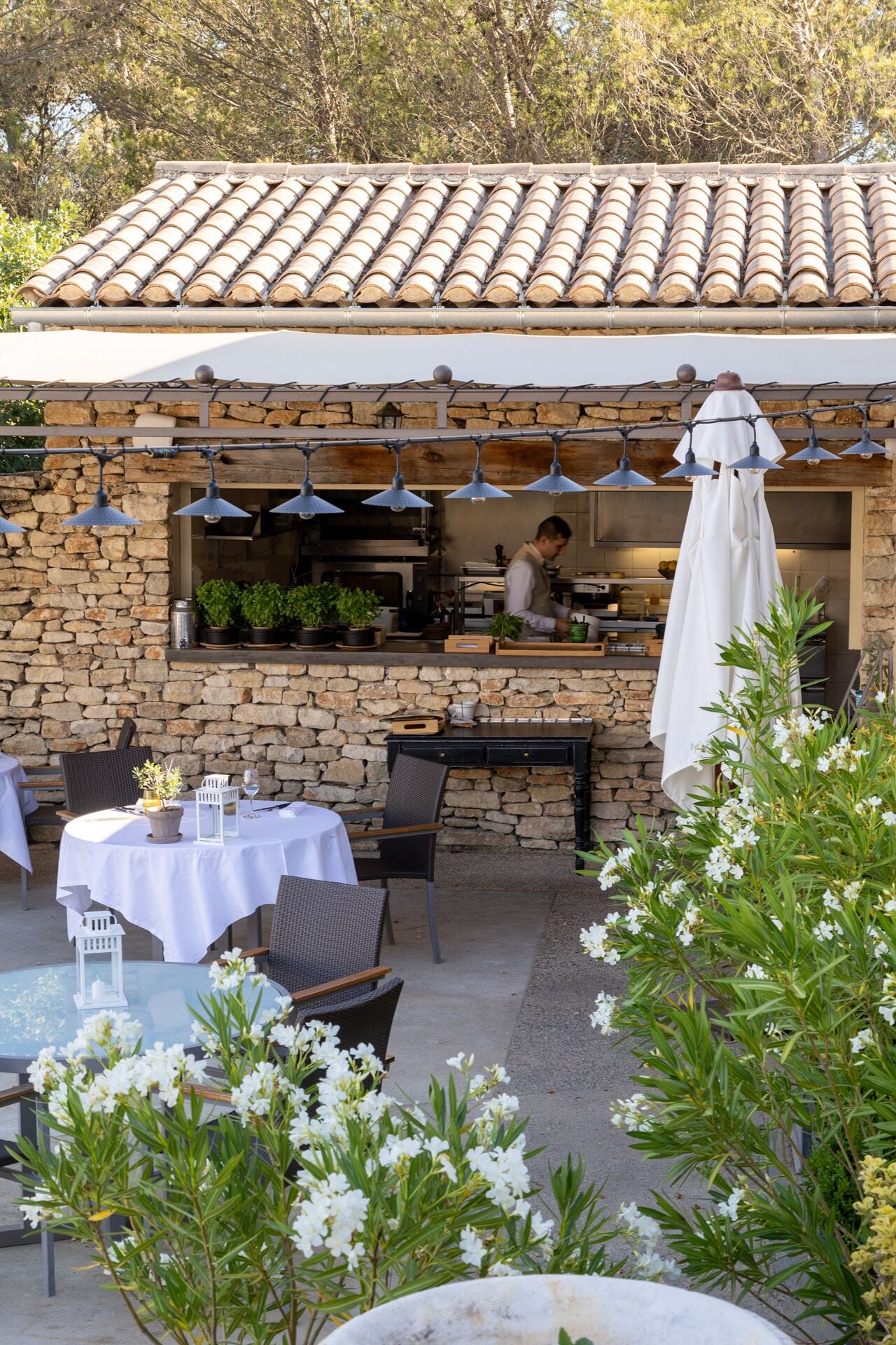 An outdoor dining area with stone walls, tables, chairs, and potted plants.