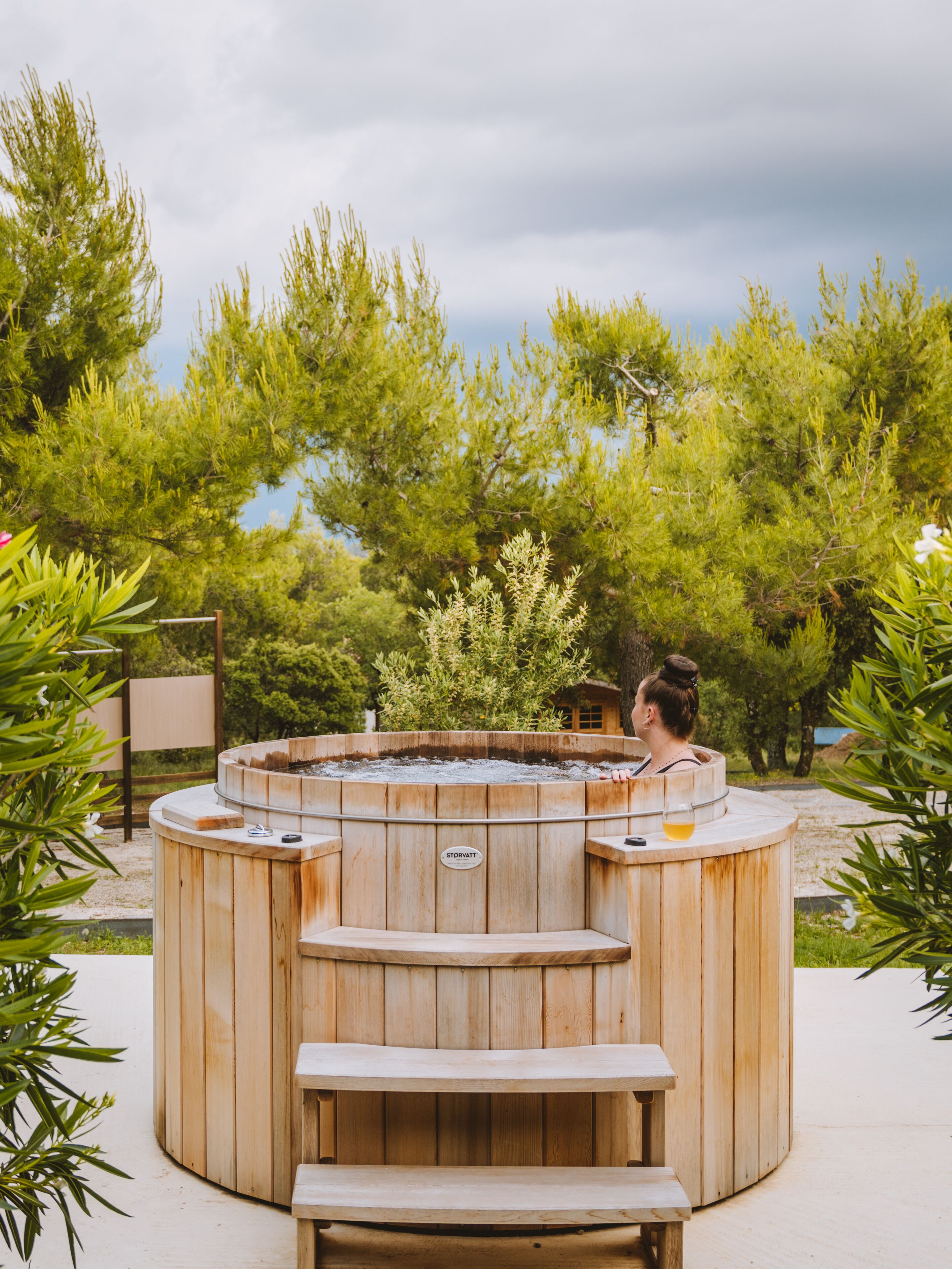 A wooden hot tub with a bench in the center, surrounded by trees.
