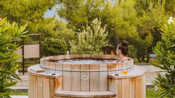 A wooden hot tub with a bench in the center, surrounded by trees.