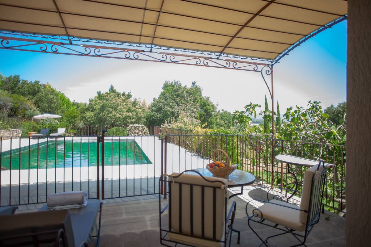 Un patio cubierto con piscina, mobiliario exterior y vistas a la vegetación circundante.