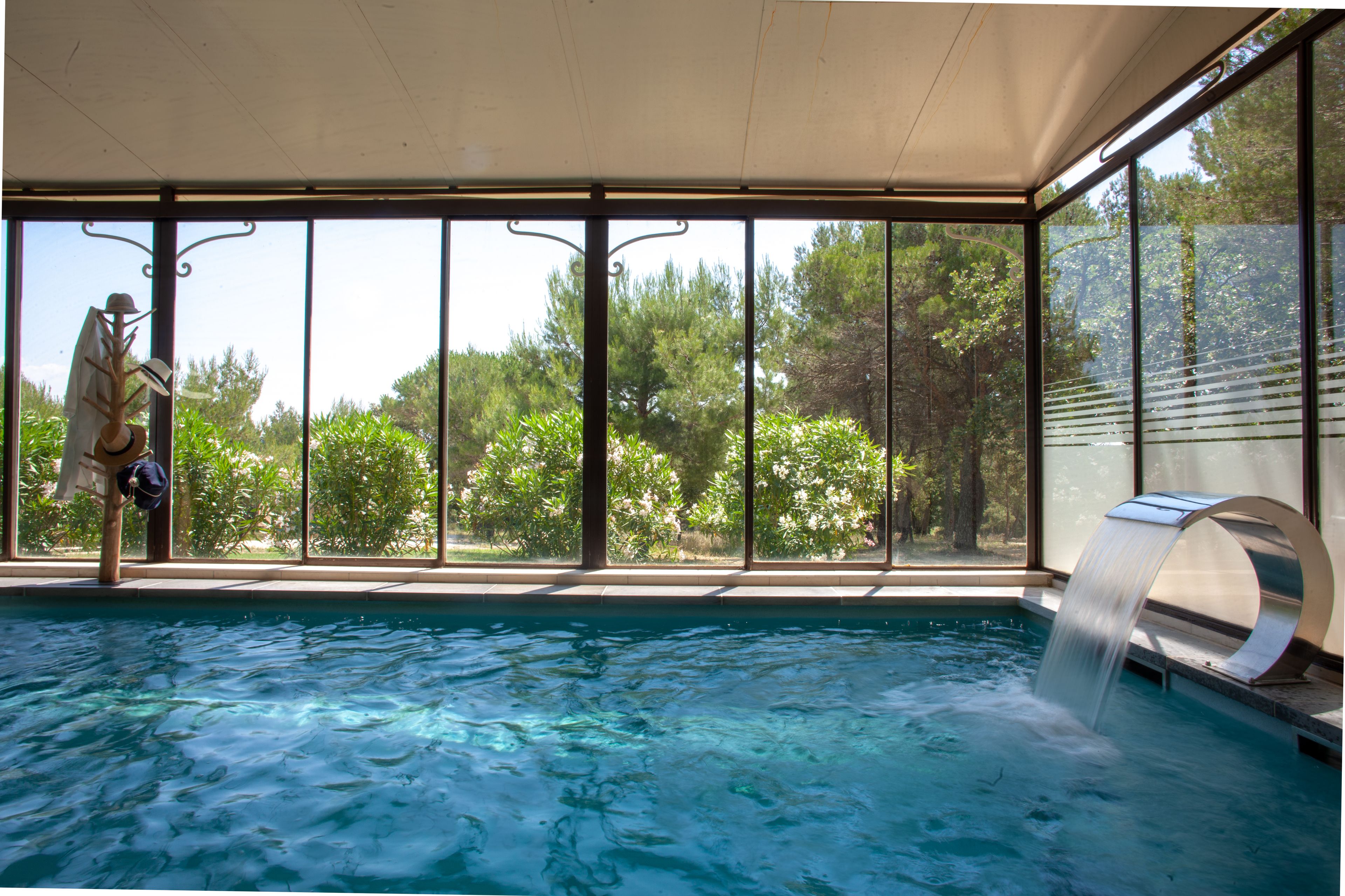 An indoor swimming pool with clear glass walls, a waterfall feature, and a statue of a person.
