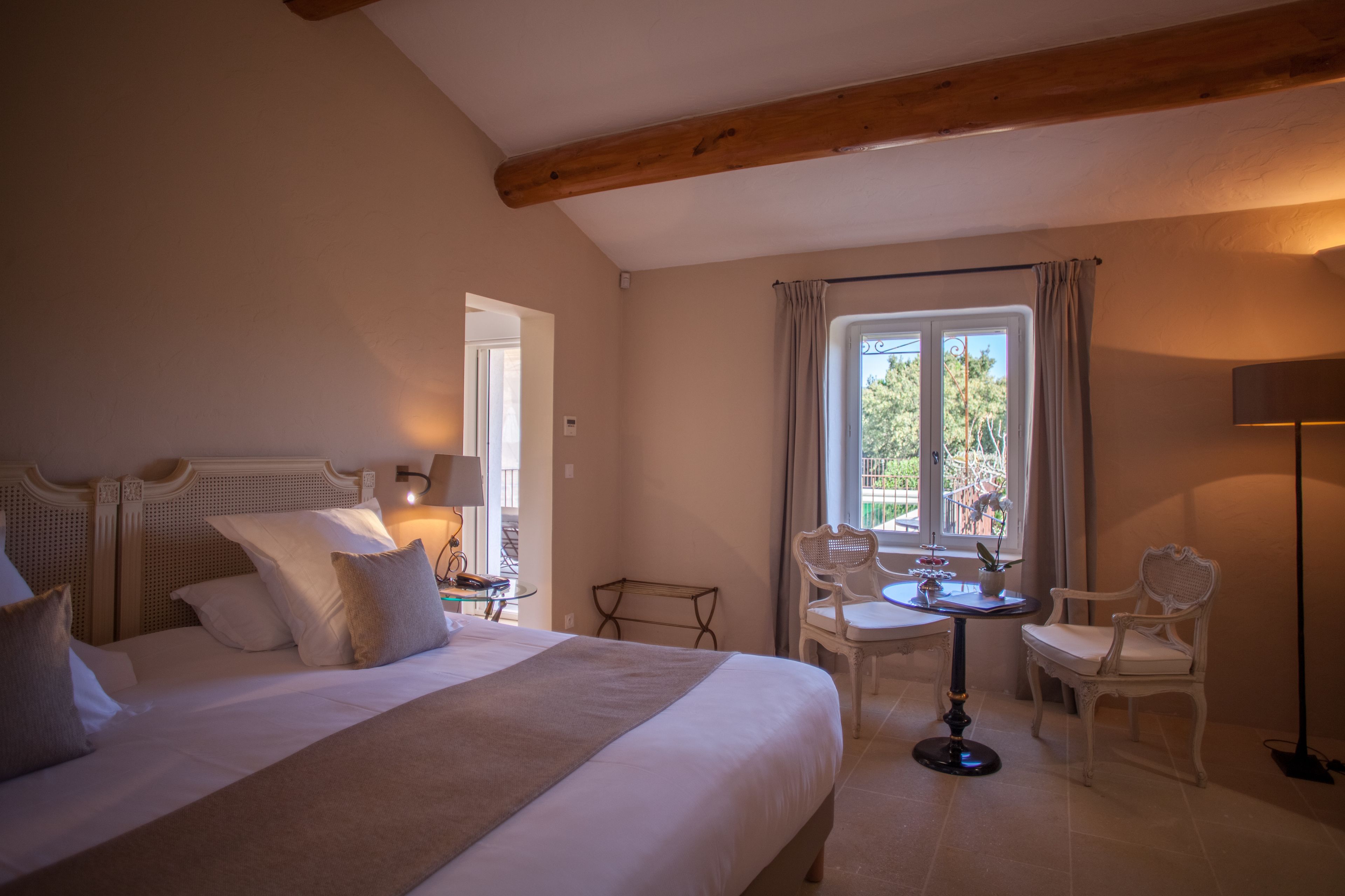 Ein Hotelzimmer mit einem großen Bett, einem kleinen Tisch mit Stühlen, einem Fenster mit Vorhängen und einer Lampe.