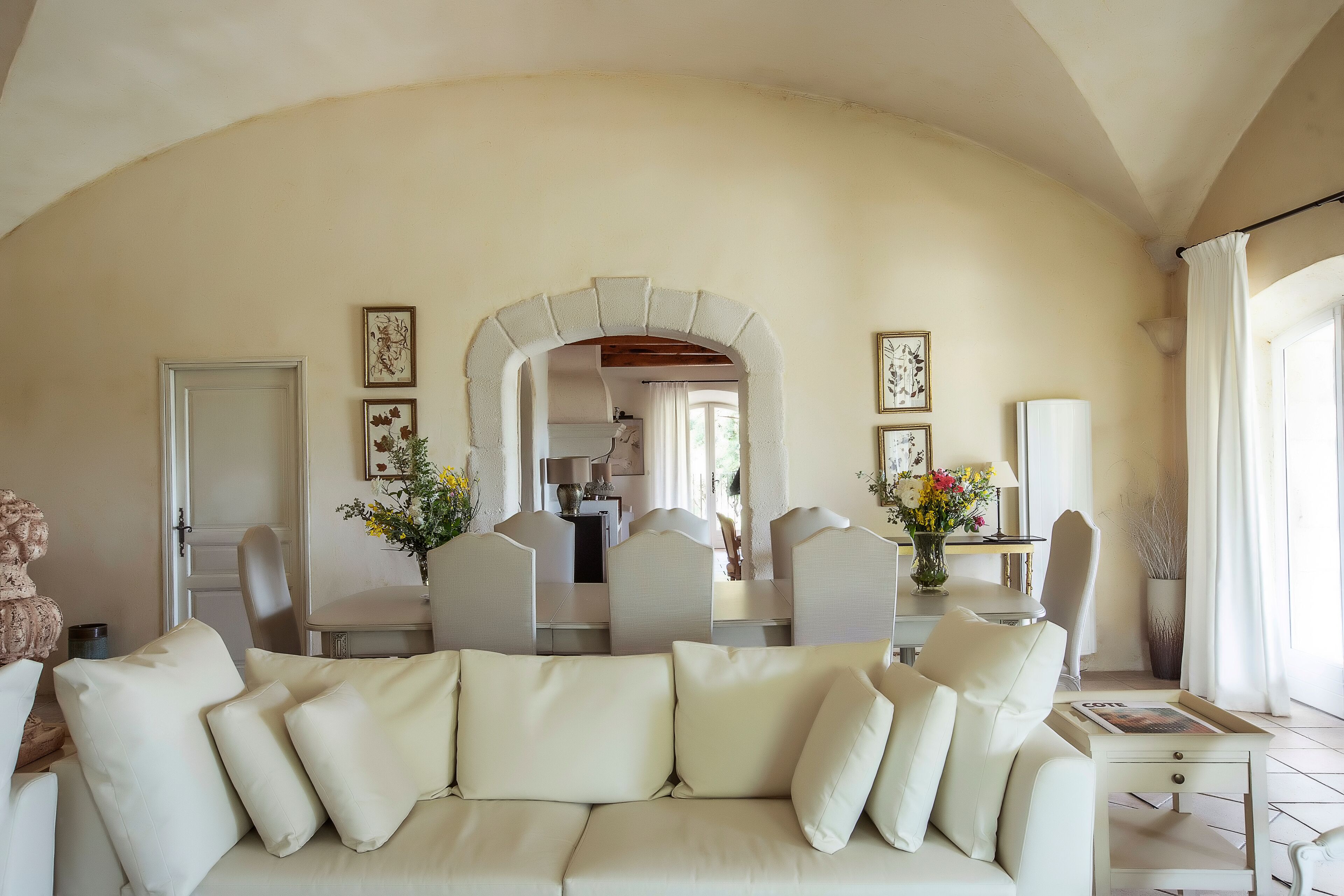 Een ruime woonkamer met een beige bank, een eethoek met stoelen, en een keuken op de achtergrond.