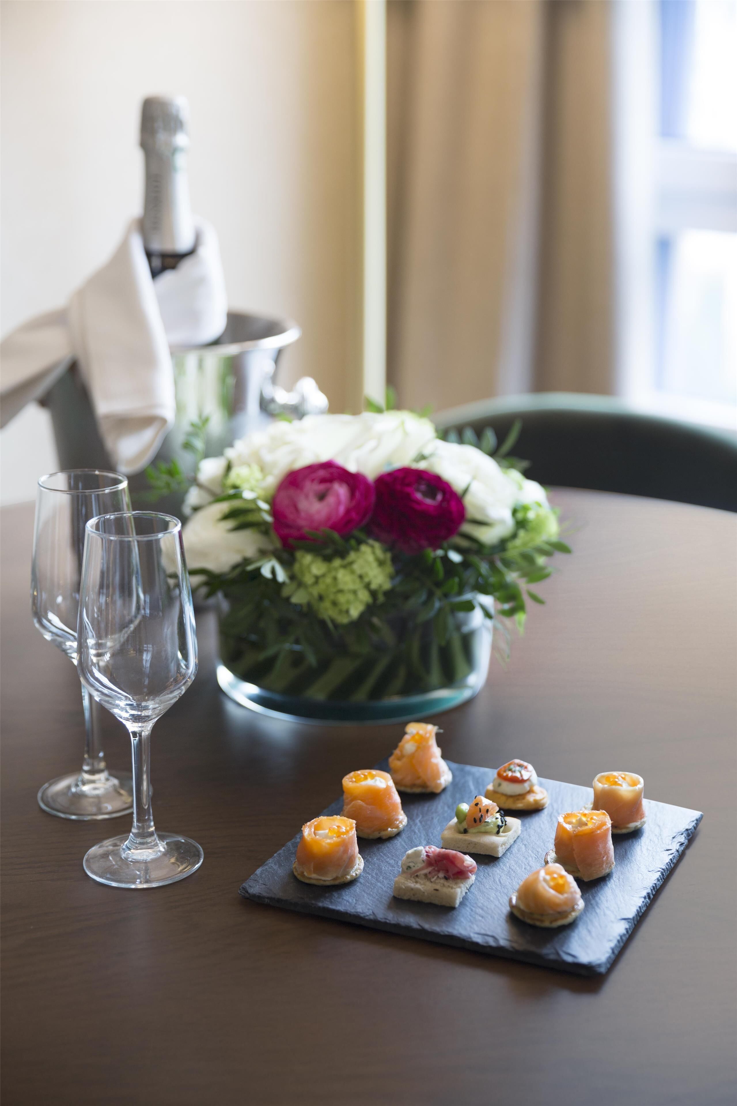 A dining table with a floral centerpiece, a bottle, and a slate board with appetizers.