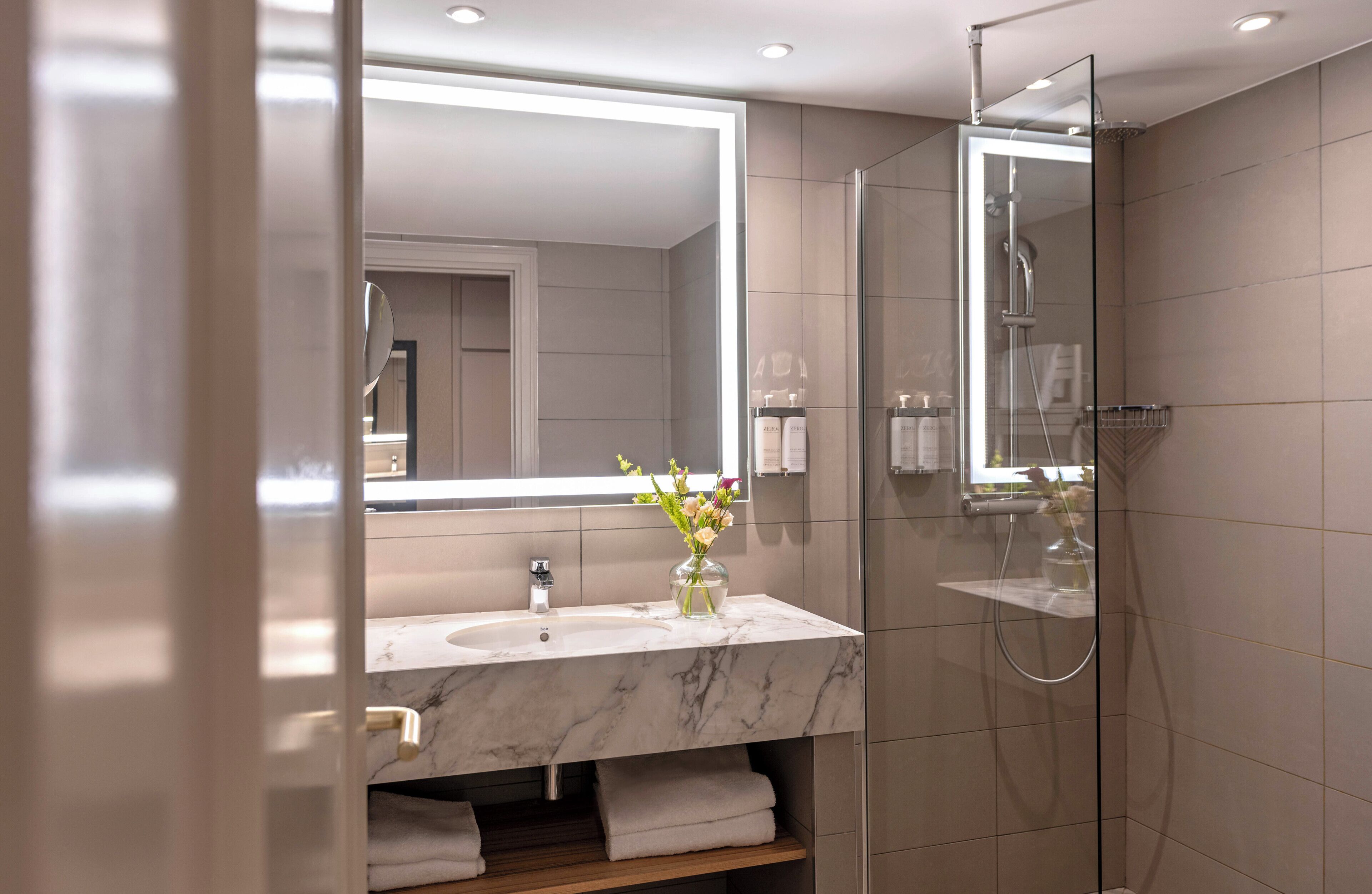 A modern bathroom with a marble sink, a glass shower enclosure, and a large mirror.