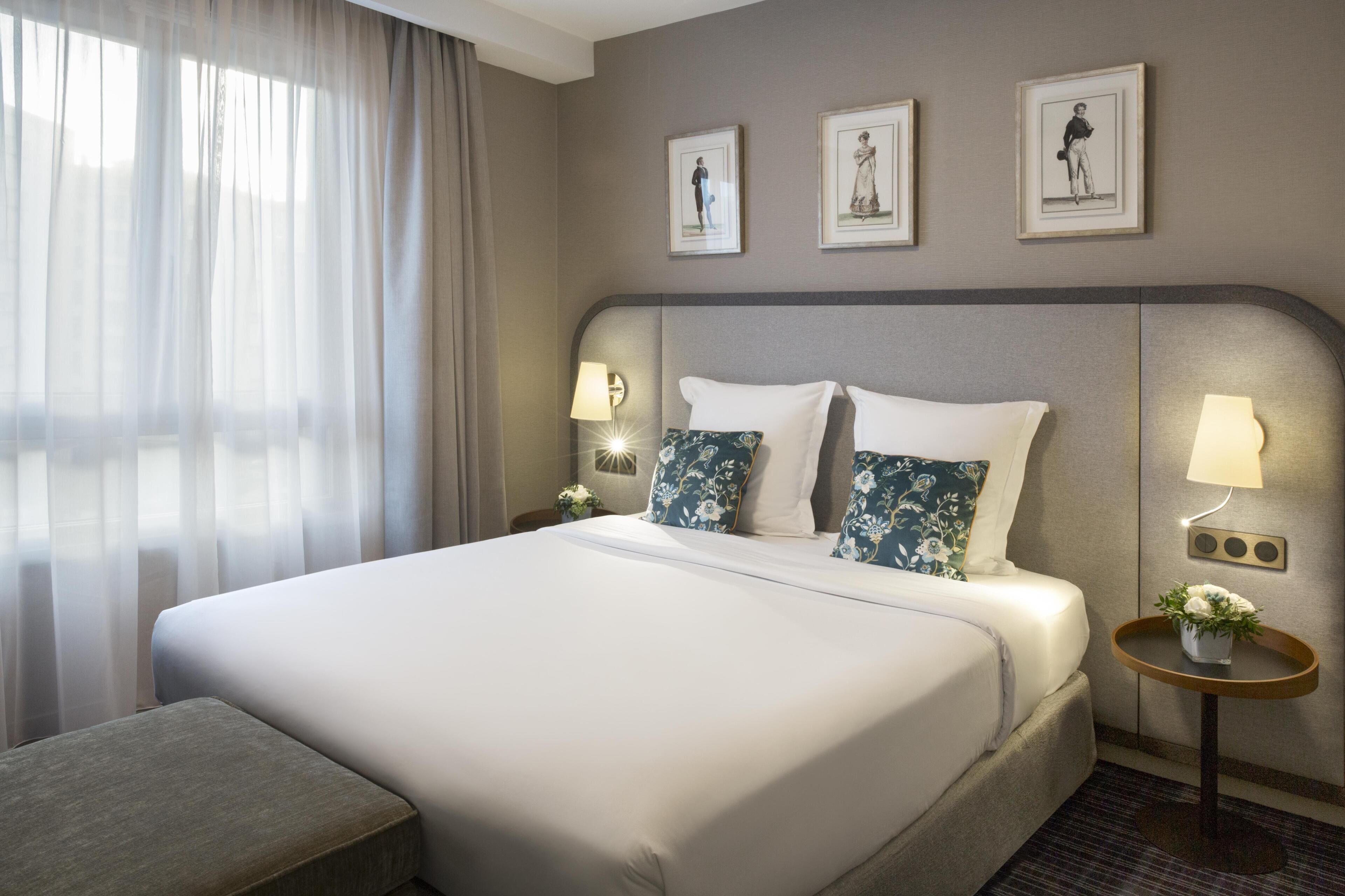 A hotel room with a large bed, two bedside tables with lamps, a small table with a vase, and three framed pictures on the wall.