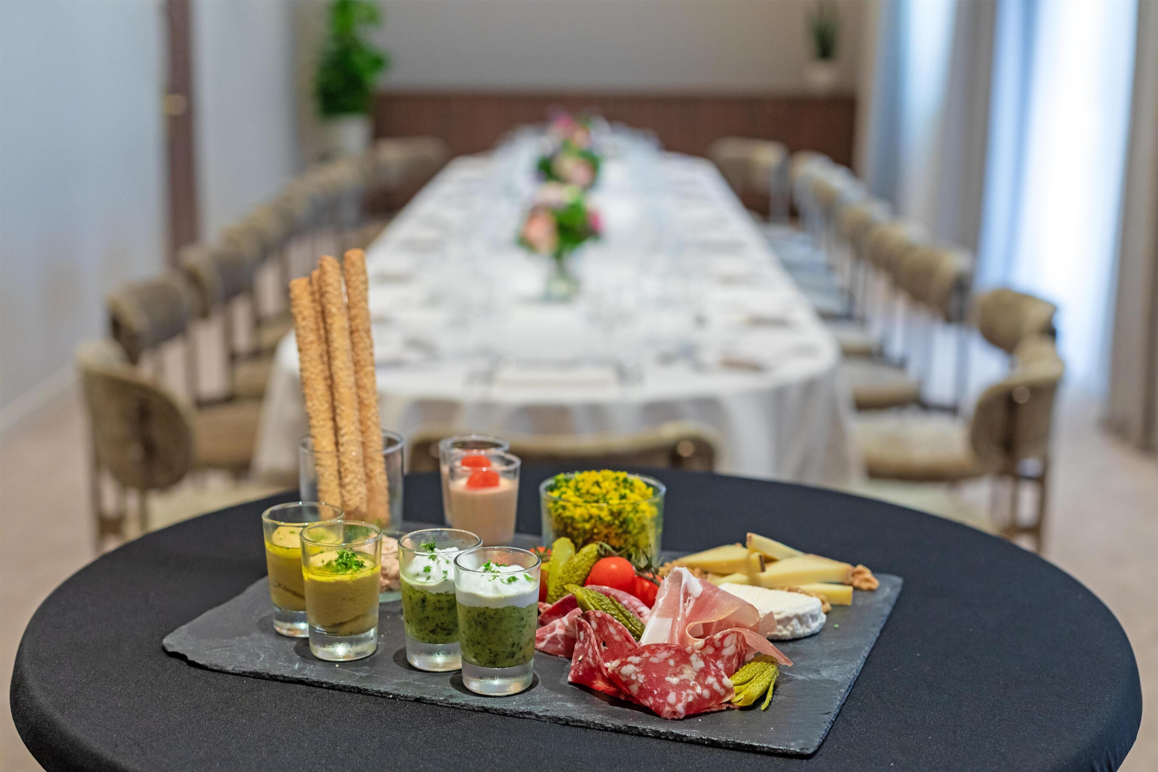 Uma mesa de jantar com diversos alimentos, incluindo queijo, enchidos e legumes.