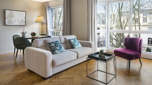 Una sala de estar moderna con un sofá, un sillón, una mesa de centro y vistas de edificios a través de amplias ventanas.