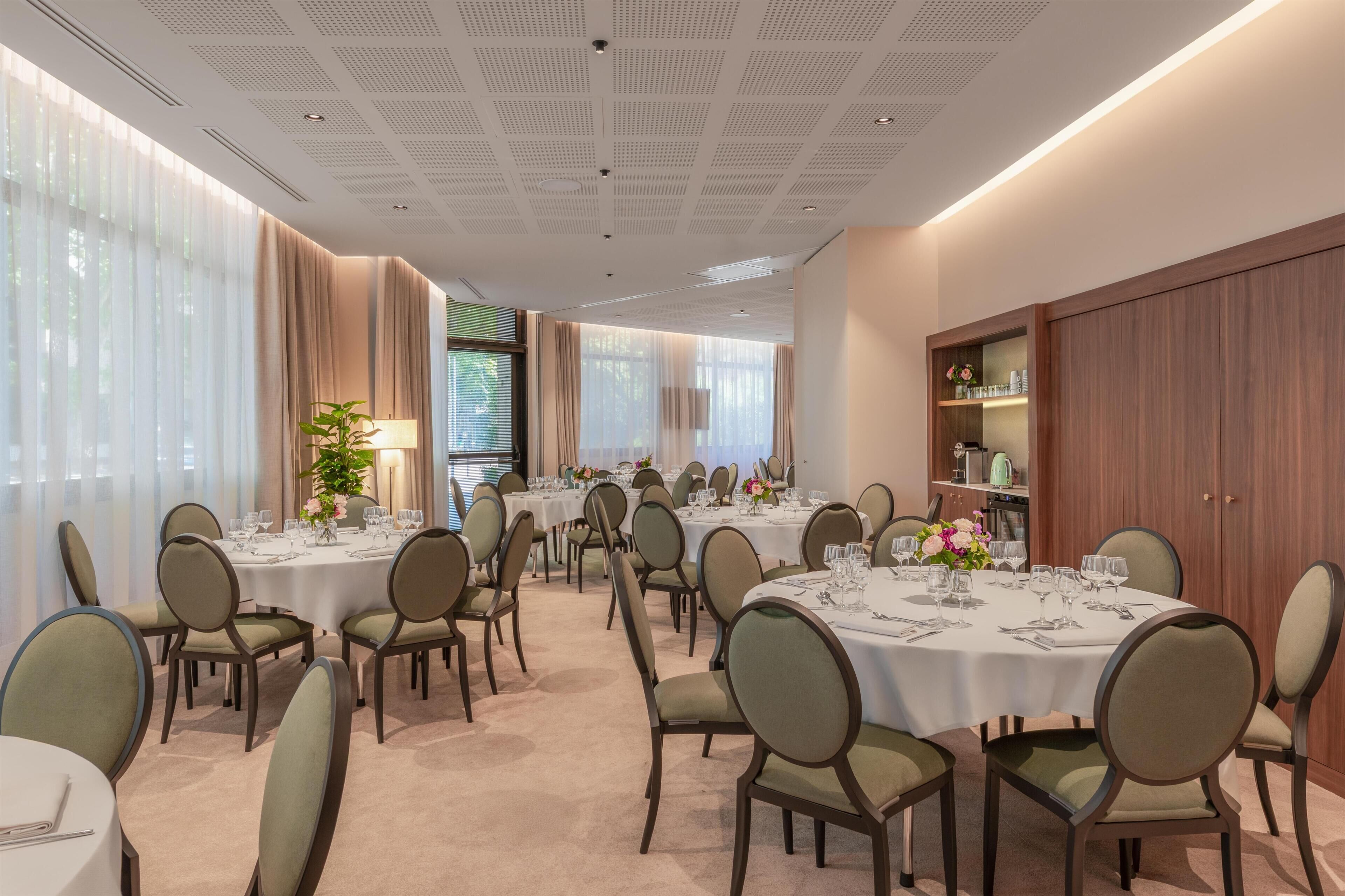 A hotel dining area with round tables, chairs, and a large window with curtains.