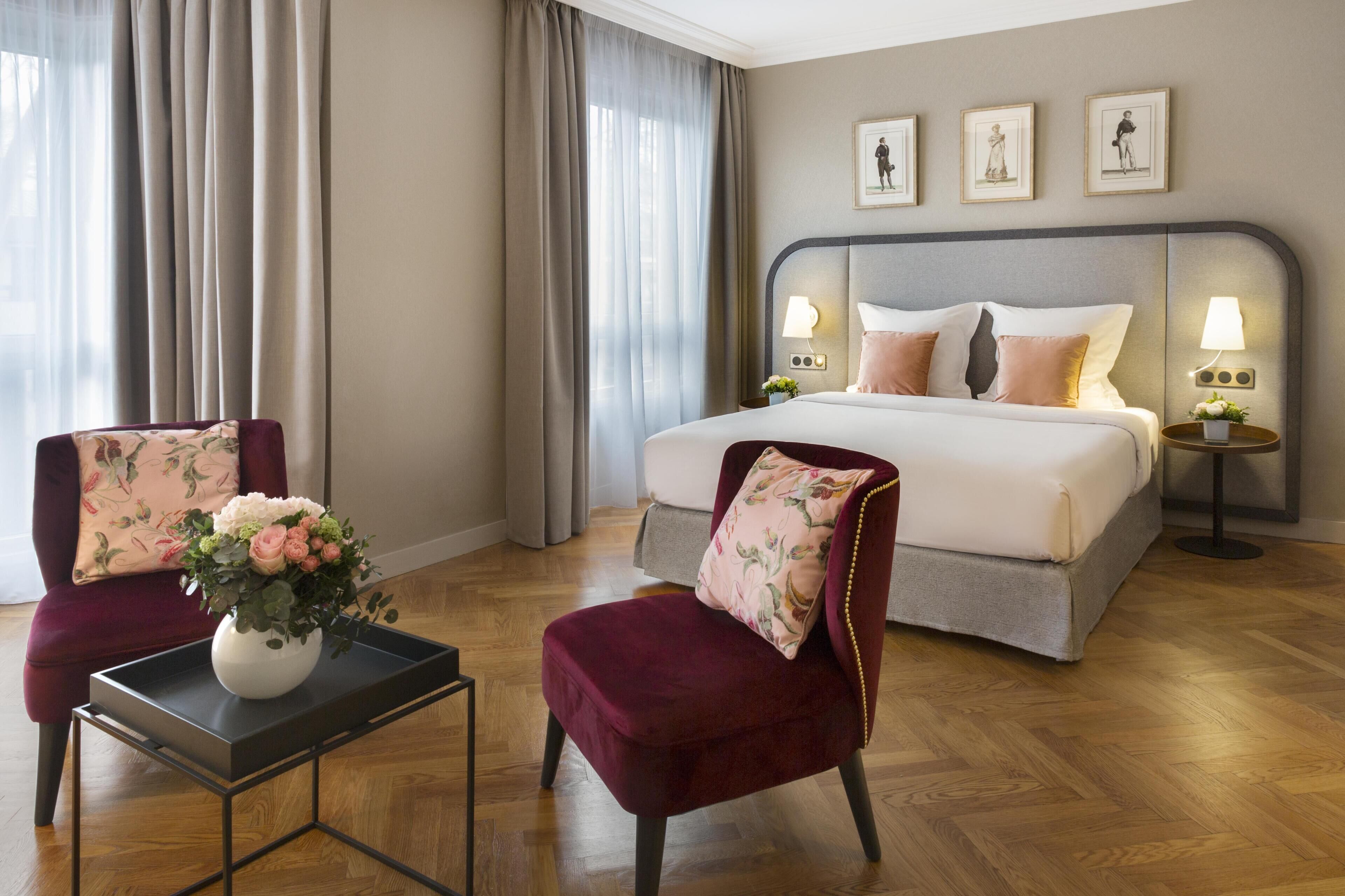 Habitación de hotel con cama, dos sillones, una mesita y una mesita de noche con lámparas.