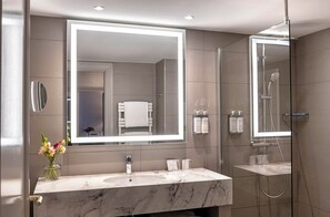 Un baño moderno con un espejo grande, lavamanos de mármol y una ducha con cerramiento de vidrio.