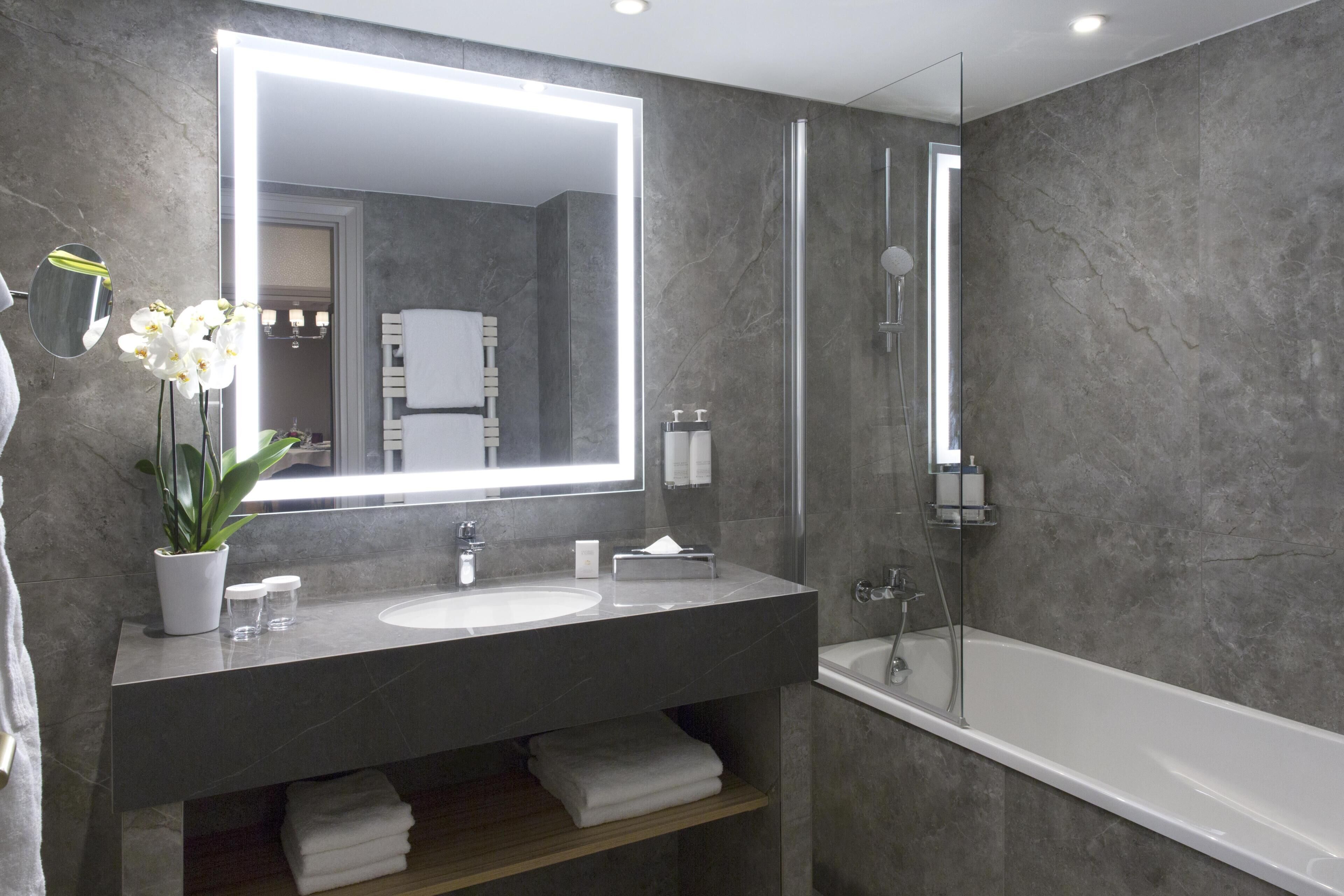 A modern bathroom with a large mirror, a sink, a shower, and a potted orchid.