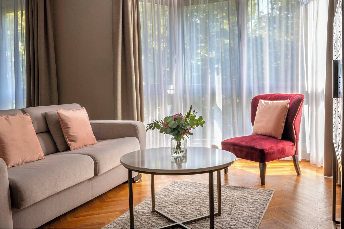 Una sala de estar con un sofá, una silla roja, una mesa de centro de vidrio y un florero con flores.
