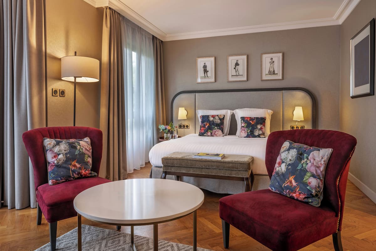 Habitación de hotel con cama, dos sillones, una mesa redonda y una mesita de noche con lámparas.