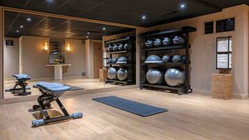A gym with exercise equipment, a yoga mat, and a wall with exercise balls.