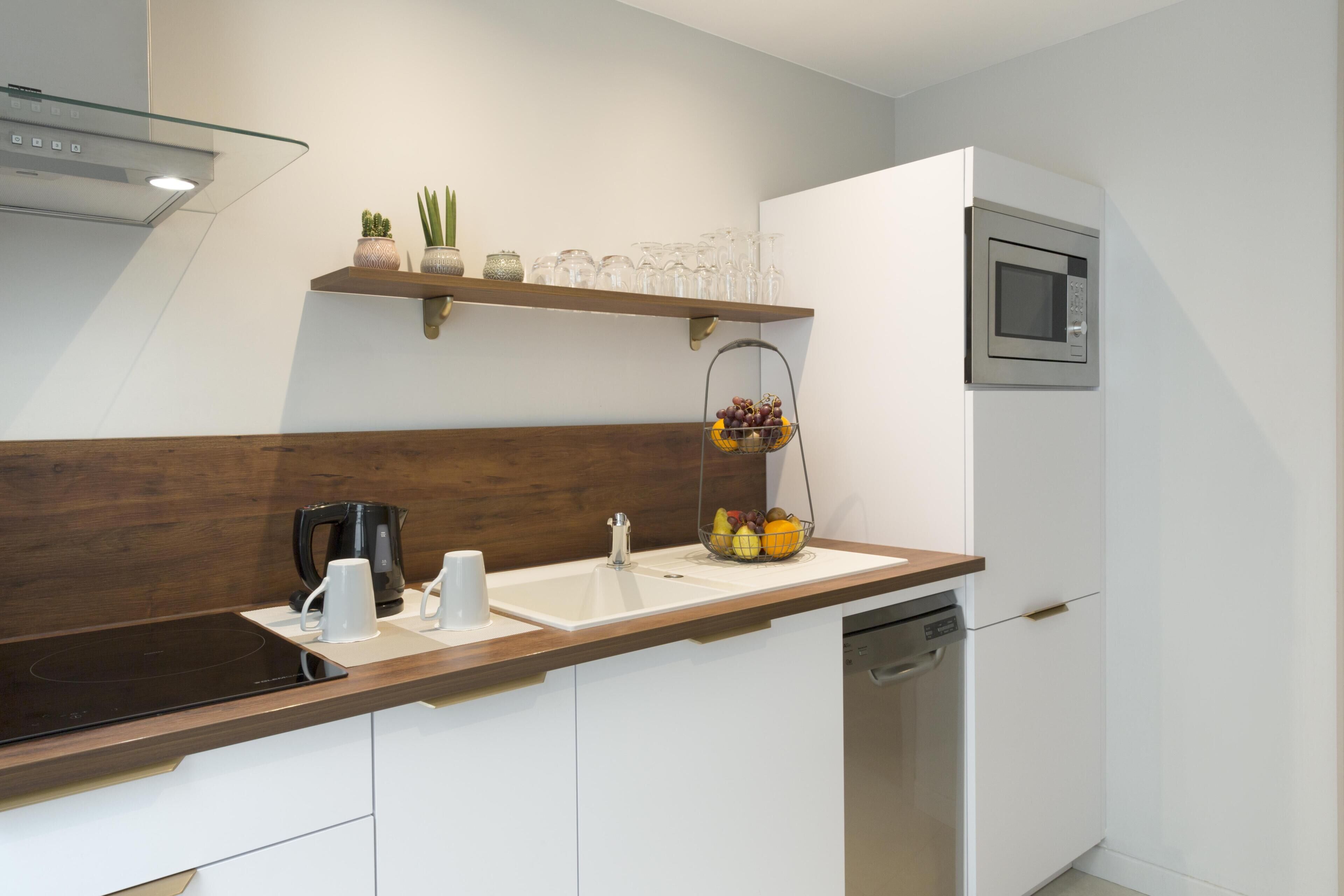 Une cuisine moderne dotée d’un plan de travail en bois, d’un lave-vaisselle encastré, d’un four à micro-ondes et d’un panier à fruits.