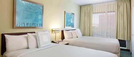 A hotel room with two beds, a nightstand, a lamp, and a window with curtains.