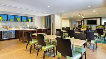 Un restaurante moderno con varias mesas y sillas, una zona de cocina y una pantalla de televisión.