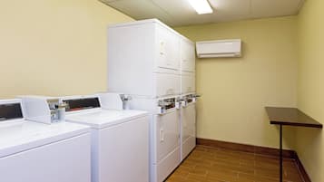 A laundry room with stacked washers and dryers, a small table, and an air conditioning unit on the wall.