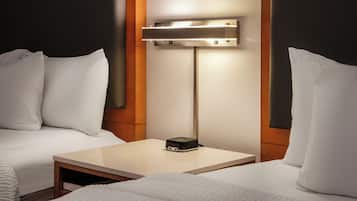 Habitación de hotel con dos camas, una mesita de noche y una lámpara fijada a la pared.