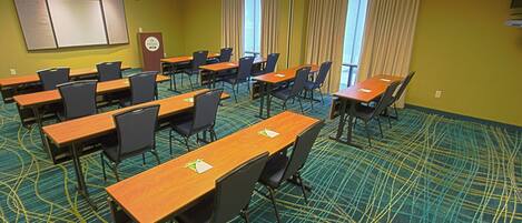 A conference room with multiple tables and chairs, a whiteboard, and large windows with curtains.