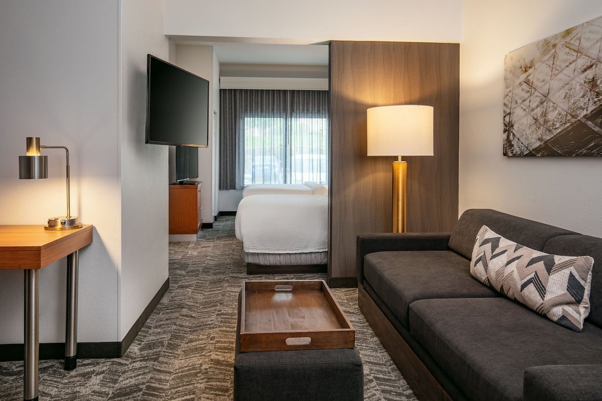 A hotel room with a bed, a sofa, a TV, a desk with a lamp, and a tray table.