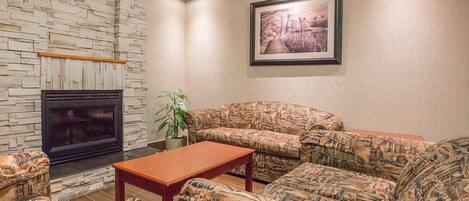 Una sala de estar con chimenea de piedra, sofás estampados, una mesa de centro de madera y un cuadro enmarcado en la pared.