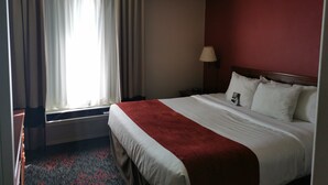A hotel room with a bed, a nightstand, a lamp, and a window with curtains.