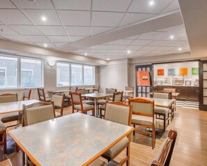A hotel dining area with multiple tables and chairs, a reception desk, and a view of the outside. - Comfort Inn & Suites Calgary - University (Calgary)