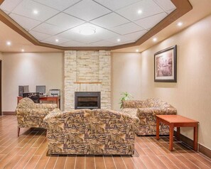 A hotel room with a stone fireplace, two patterned sofas, a wooden table, and a desk with computers. - Comfort Inn & Suites Calgary - University (Calgary)