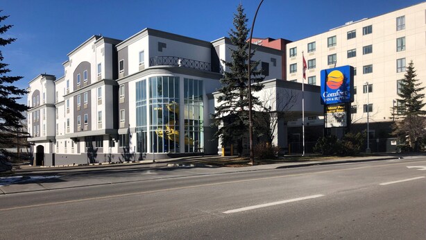 Un hotel moderno con una amplia fachada de vidrio, un llamativo letrero Comfort Inn & Suites y un cielo azul despejado.